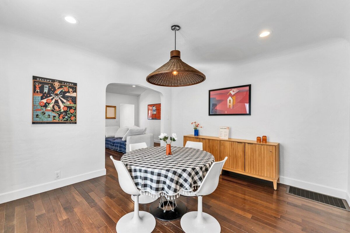 Dining area with tulip chairs, gingham-topped round table, and gallery art — Atwater Village